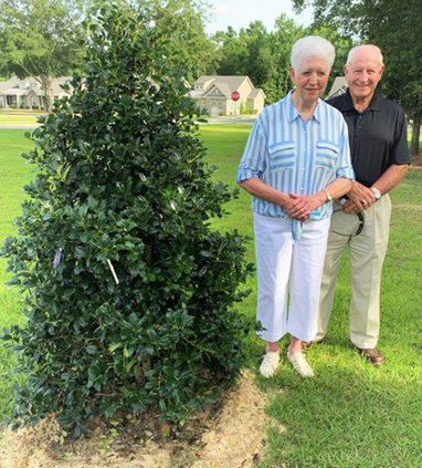 Janelle Rushing Hughes stands next to the Robin Holly tree planted on the front lawn of The Lodge at Bethany in her honor.
