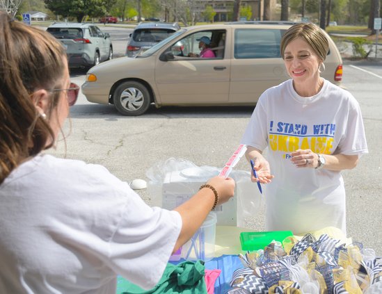 Meaghan Black, left, passes off some raffle tickets to Illona Fountain as donor Nan McPhatter waits in her vehicle during a fundraising drive led by Fountain to help assist people in Ukraine and those who have fled the war there at Pittman Park United Met