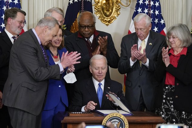 President Joe Biden signs the Postal Service Reform Act of 2022 in the State Dining Room at the White House in Washington, Wednesday, April 6, 2022. Watching from left are Sen. Gary Peters, D-Mich., Senate Majority Leader Chuck Schumer of N.Y., Sen. Rob P