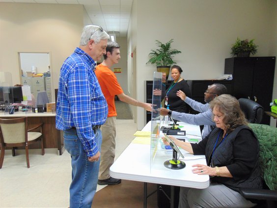 Bulloch County residents Jeff Smith IV, left, and Jeff Smith V, in orange shirt, check in as early voters Thursday afternoon at the Board of Elections and Registration office in the County Annex on North Main Street, Statesboro. From right, poll worker Ma