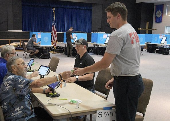 In this file photo from November 2022, after checking in at the Pittman Park precinct, Bradley Sapp, right, receives his voting machine card from Poll Manager Bob Marsh. Citizens wanting to vote in Georgia’s May 21 general primary and nonpartisan general