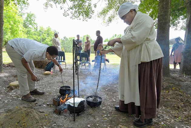 In this photo from the 2023 "A Taste of Struggle" event, Chef Alex Curtis, left, stirs some onions, while food historian Clarissa Clifton heats water with a white-hot canon ball. The duo teamed up to make Hoppin' John over an open fire with well-seasoned