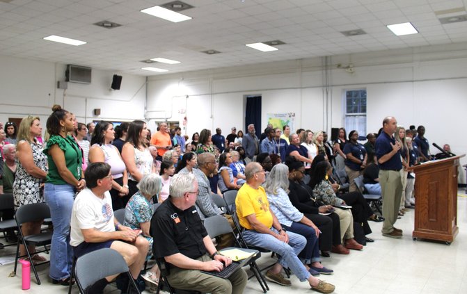 Teachers attending Wednesday's special meeting of the Bulloch County Board of Education stand at the request of Transitions Learning Center Administrator Tim Rountree, at lectern, as he speaks for keeping the TLC open and not cutting teaching jobs.