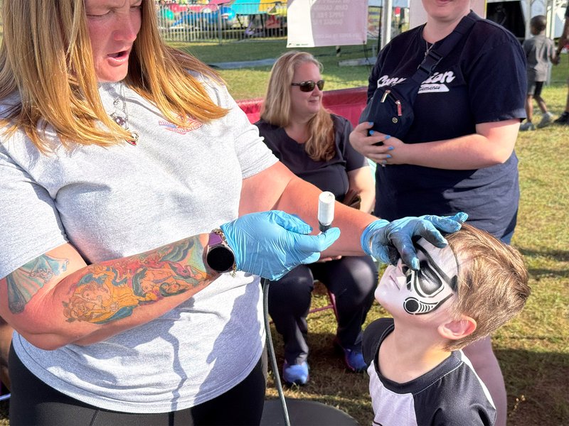 Carnival midway artist Erica Guzman puts the final touches on the face paint for Jameson Barthelmew of Statesboro